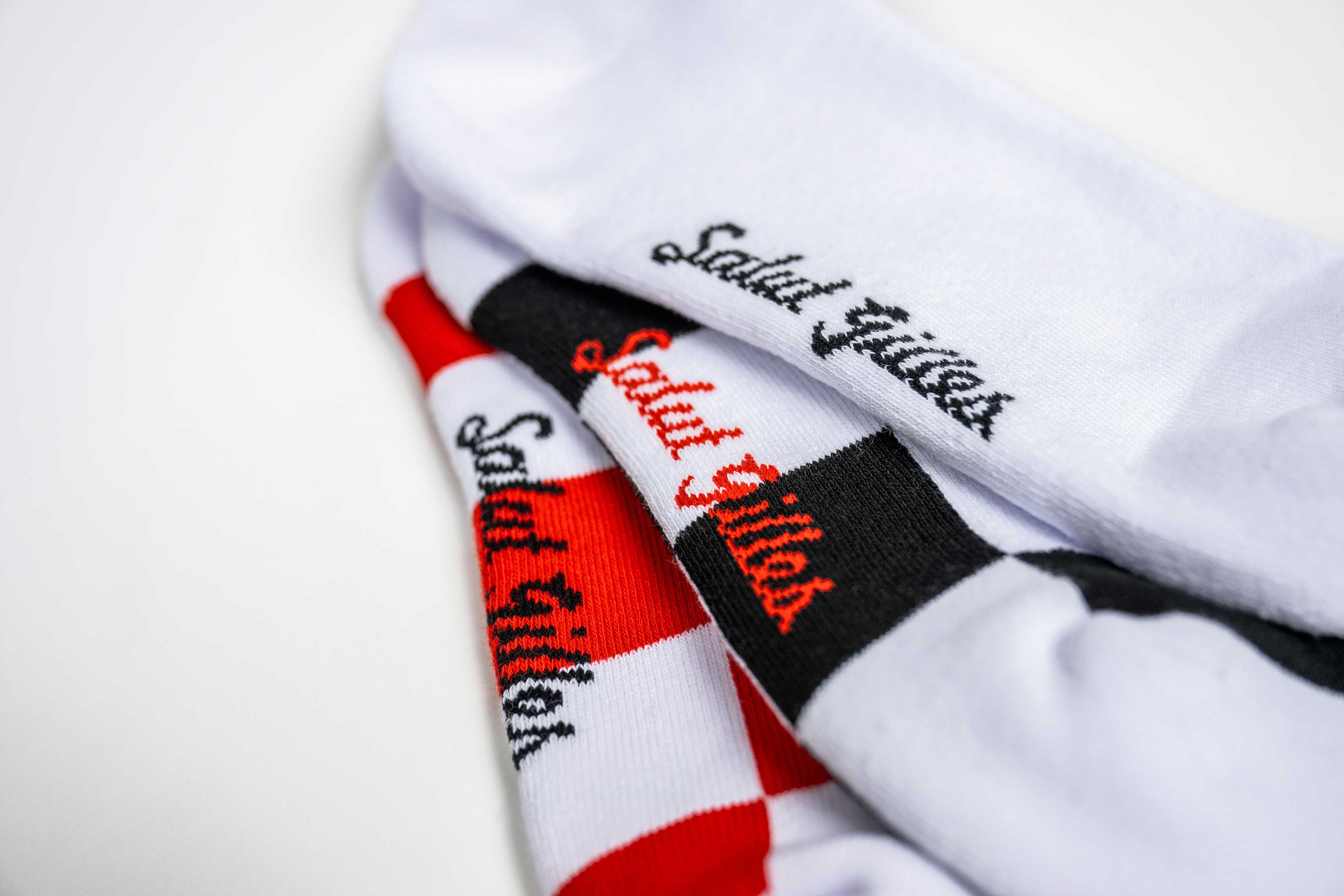 Gros plan sur des bas blancs CGV avec inscription rouge ‘Salut Gilles’ et motif damier rouge.