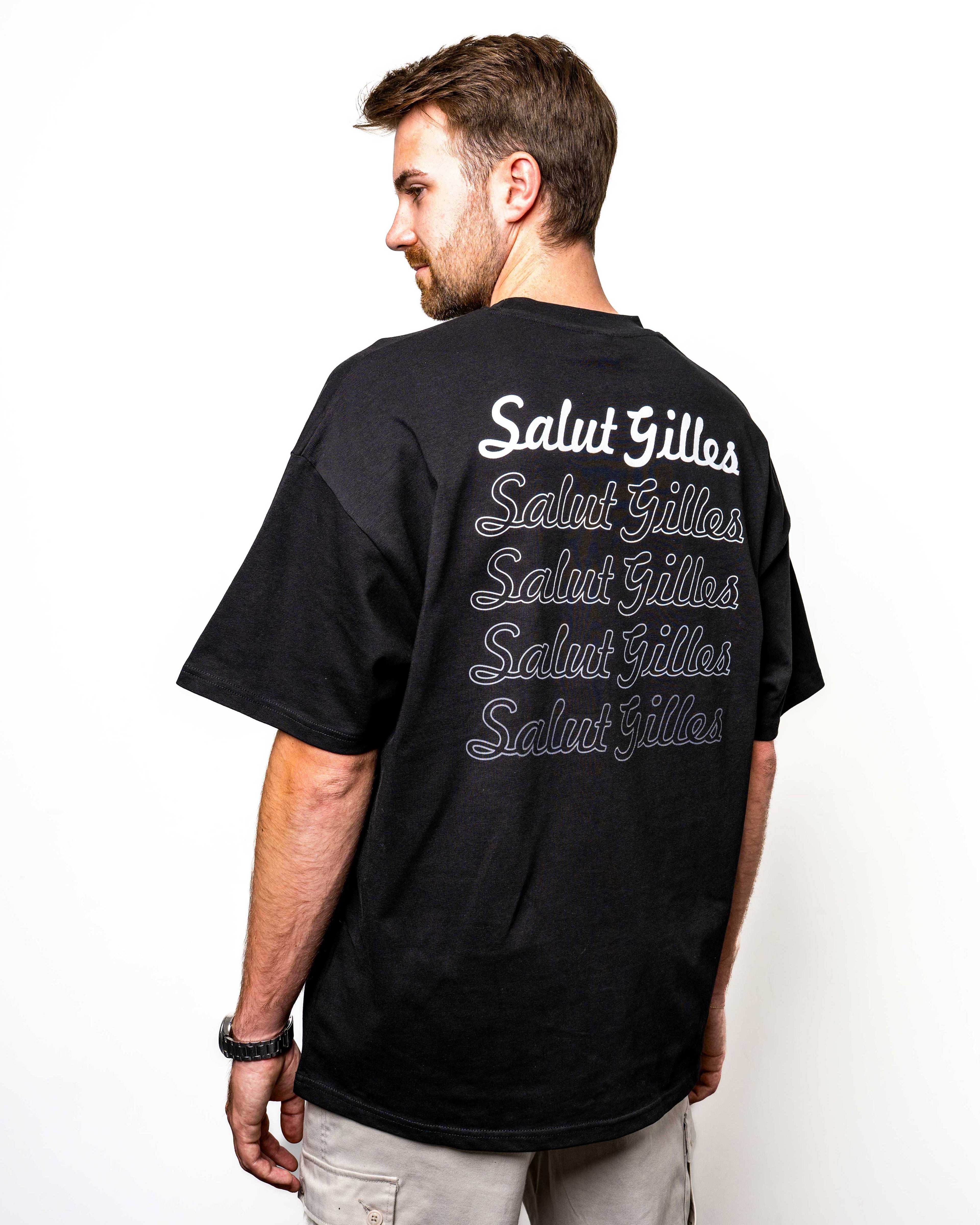 Modèle homme de dos avec le t-shirt noir ‘Salut Gilles’, coupe oversize et texte commémoratif.