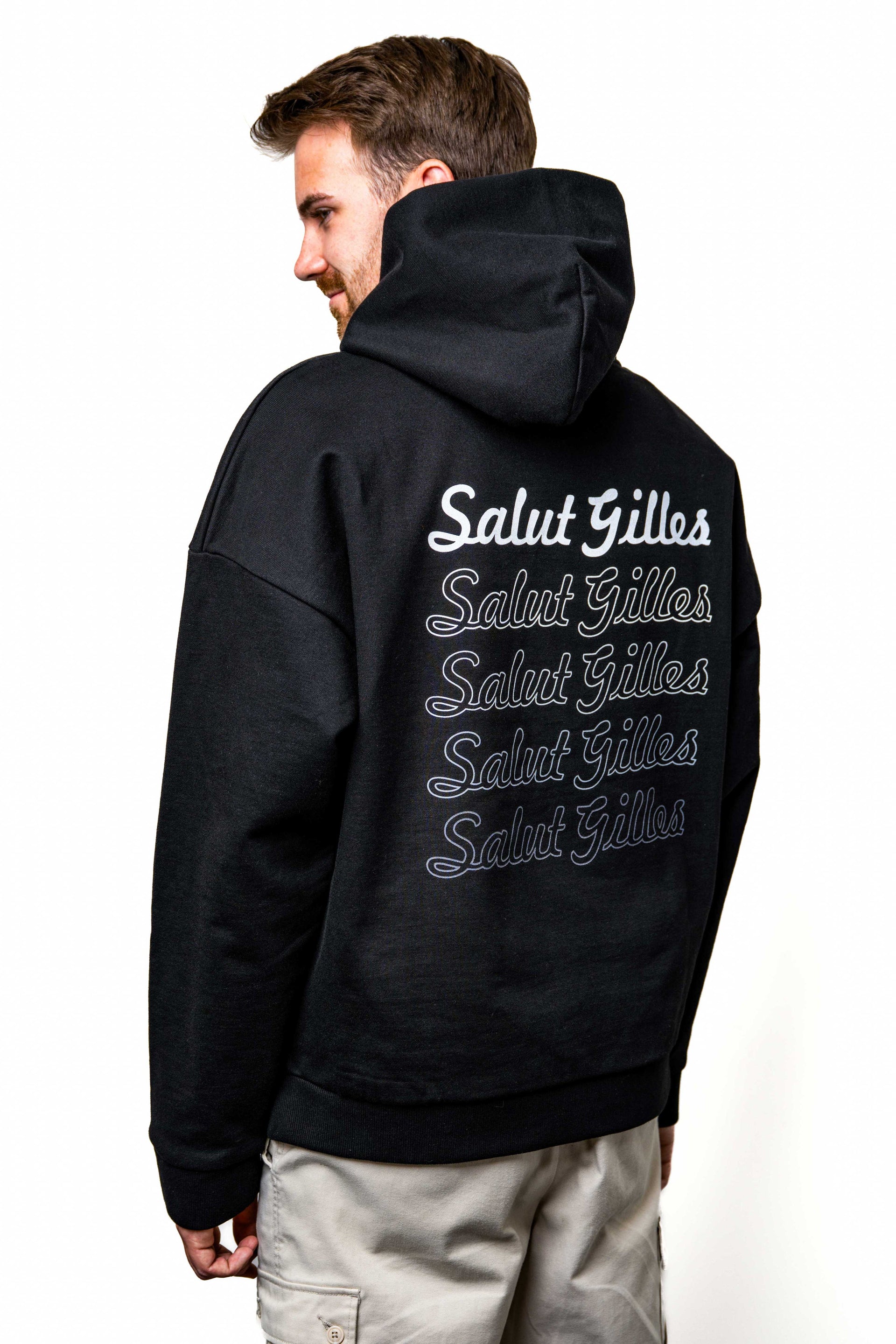 Modèle homme portant le hoodie noir ‘Salut Gilles’, vue de dos montrant l’inscription commémorative en blanc.