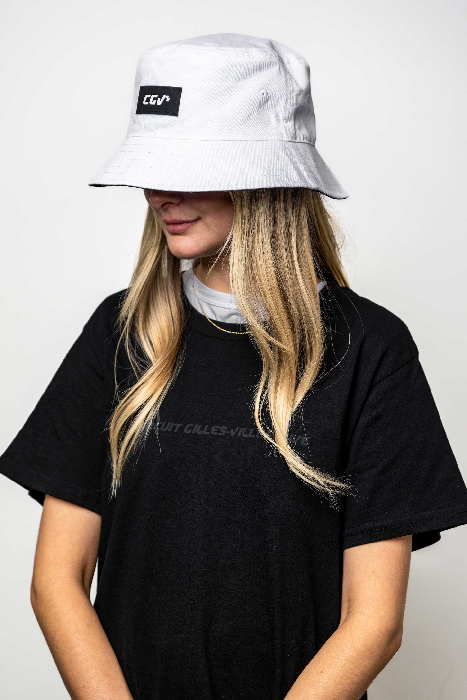  Modèle femme portant un t-shirt noir ‘Winner’, avec chapeau blanc, vue de trois quarts.
